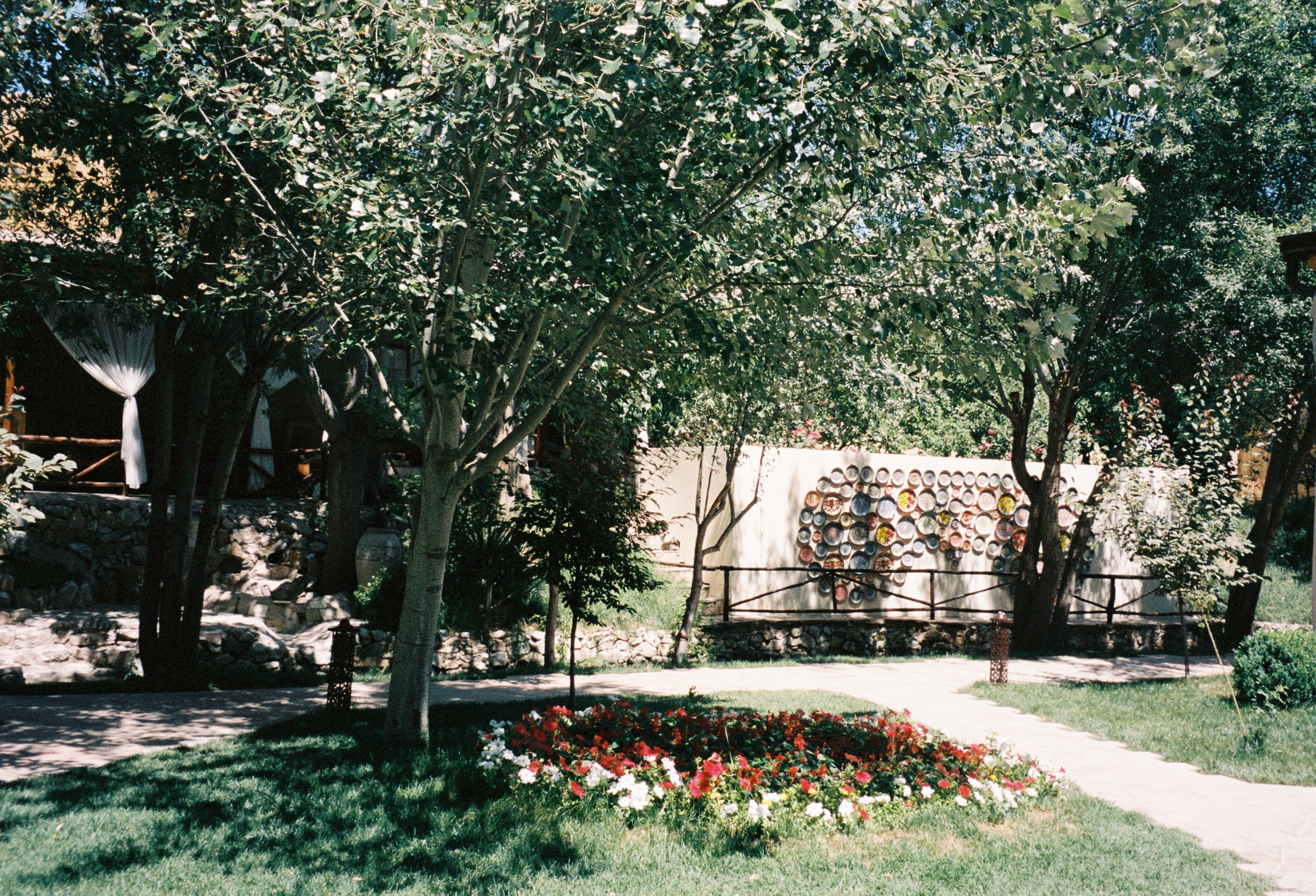 Garden with flower beds and decorative ceramic plates on the wall at Meros Paper Mill, Konigil village, Samarkand, Uzbekistan — film photography by Loud Etudes